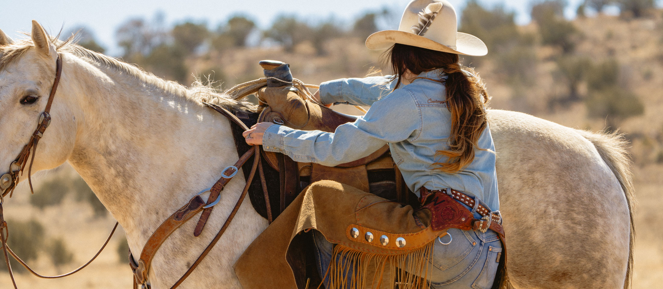 A cowgirl climbing onto a horse.